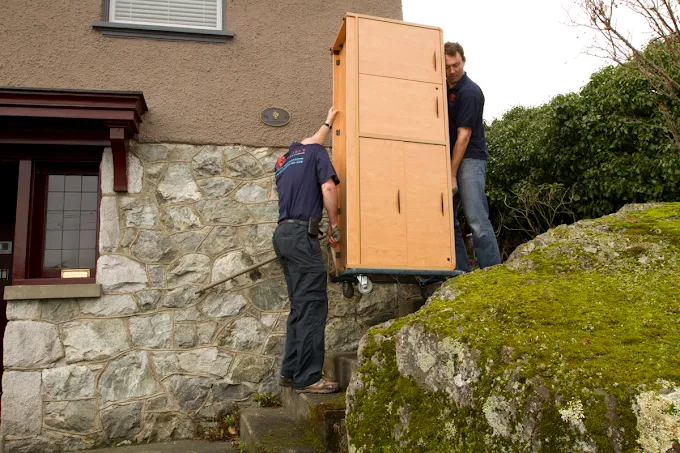 Foster's movers carrying a cabinet over outdoor steps